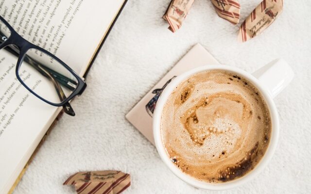 Coffee, glasses, and a book laying on a table.