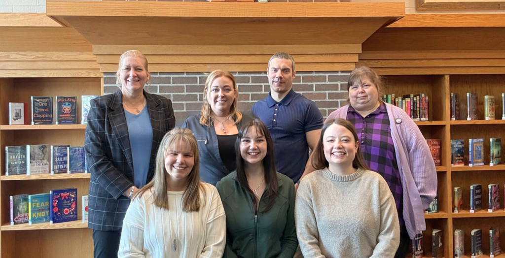 Library staff members smiling in front of the fireplace
